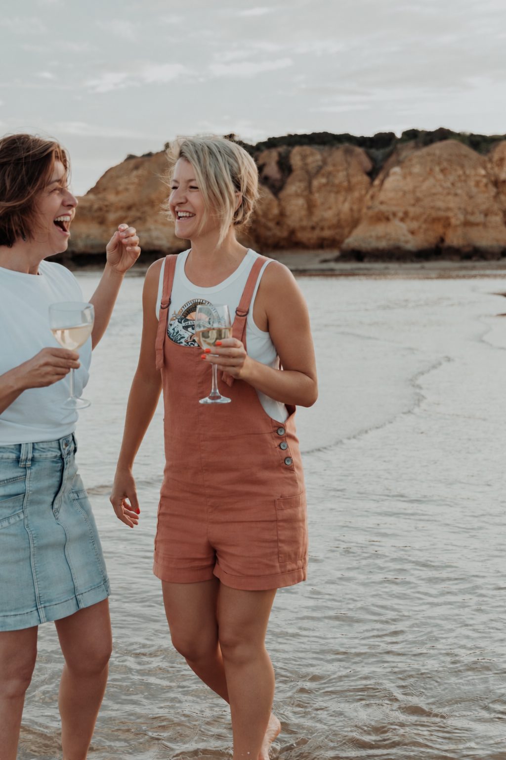 Alana laughing with a friend at the water’s edge on the Surf Coast
